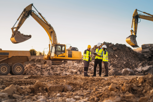 Construction workers discussing project plans on a mining site with excavators in the background
