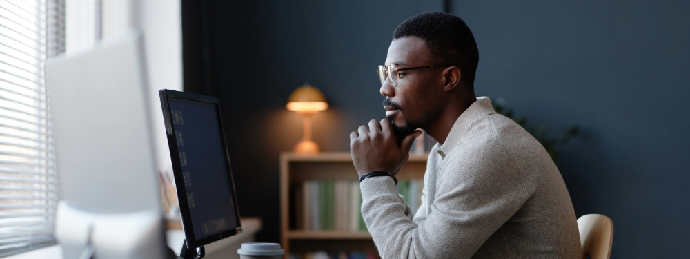 IT professional reflecting on work habits while using a computer in a modern office.