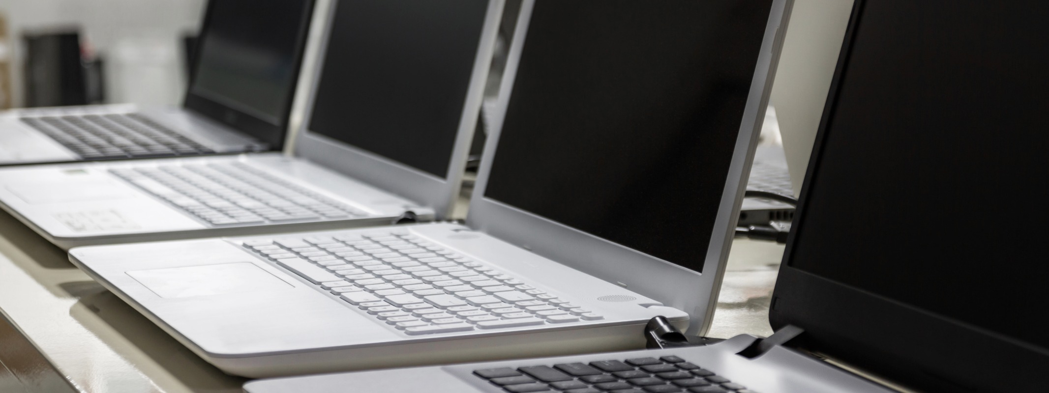 Row of identical business laptops on a desk, representing standardised IT hardware procurement.